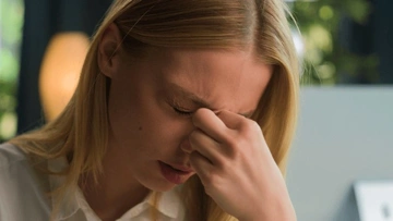 A young woman with blonde hair showing a distressed expression while rubbing her forehead.