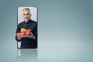 A chef holding a plate of vegetables displayed on a smartphone.